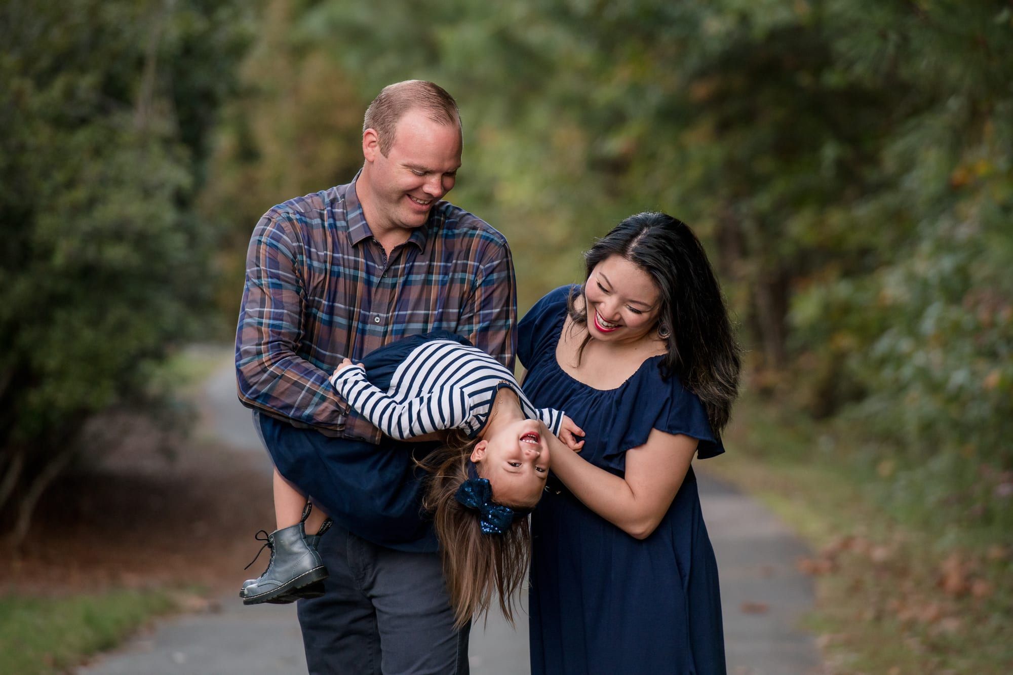 Parents swinging their laughing daughter upside down on a wooded path